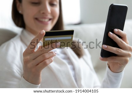 Close up smiling young woman using phone, holding plastic credit card, making secure internet payment, entering information, browsing banking service, checking balance, girl shopping in internet