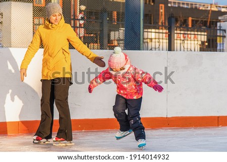 Mom teaches little daughter to skate, winter evening at sunset