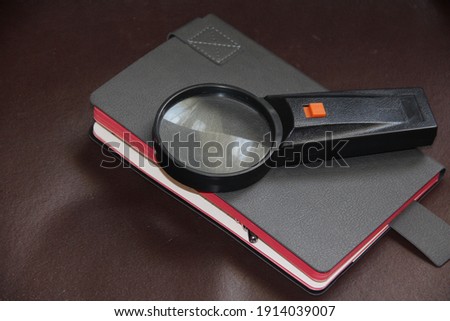 the gray notebook, magnifying glass on a dark background
