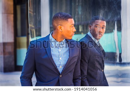 A young black businessman is standing by a mirror on the street and looking at the reflection. Concept of self assured, self esteem and self checking. A fine art lifestyle color photography. Royalty-Free Stock Photo #1914041056