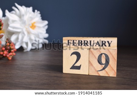 February 29, Date cover design with calendar cube and white Paeonia flower on wooden table and blue background.