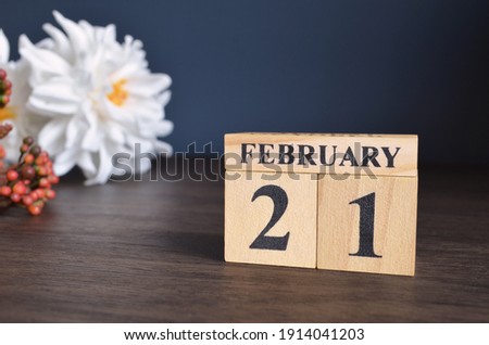 February 21, Date cover design with calendar cube and white Paeonia flower on wooden table and blue background.