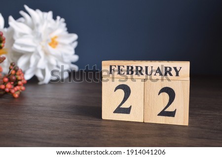 February 22, Date cover design with calendar cube and white Paeonia flower on wooden table and blue background.