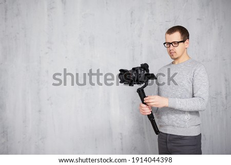 professional videographer shooting video using modern dslr camera on 3-axis gimbal over grey concrete wall background with copy space