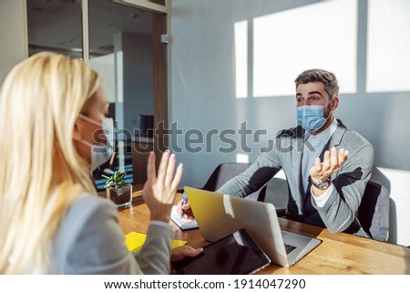 Business people with face masks sitting at the office and having a meeting during coronavirus. Colleagues talking about job improvement. Collaboration, interview, COVID 19 measure Royalty-Free Stock Photo #1914047290