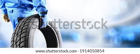Mechanic holding tire with copy space for text repair service center, blurred background, Maintenance transport  panorama or banner photo. Royalty-Free Stock Photo #1914050854