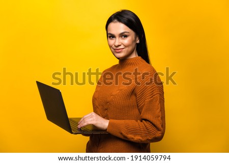 Charming satisfied young caucasian smiling woman in casual sweater, stands on isolated orange background, holds and uses, looks and smiles at the camera