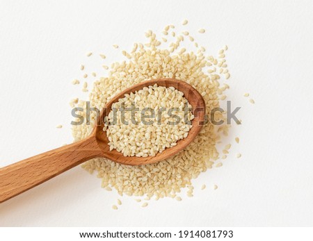 White sesame seeds in wooden spoon on pile of white sesame seeds, top view. Royalty-Free Stock Photo #1914081793