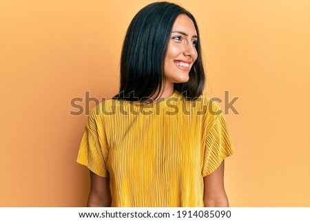 Young brunette woman wearing yellow tshirt over yellow background looking to side, relax profile pose with natural face and confident smile.  Royalty-Free Stock Photo #1914085090