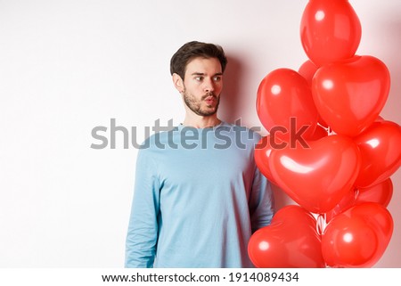 Relationship. Young man looking confused at heart balloon, puzzled on valetines day, standing over white background Royalty-Free Stock Photo #1914089434