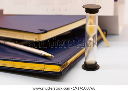 blue leather notebooks , hourglass and a pen. Preparing for a business meeting. Business concept