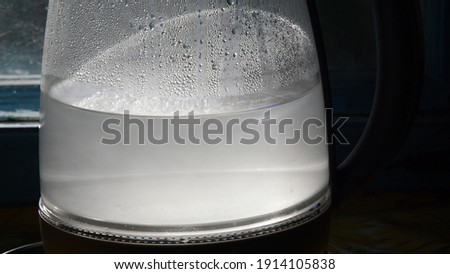 Turbid water inside misted glass teapot with shiny drops in bright sunlight. Closeup of boiled water in old transparent kettle on kitchen Royalty-Free Stock Photo #1914105838
