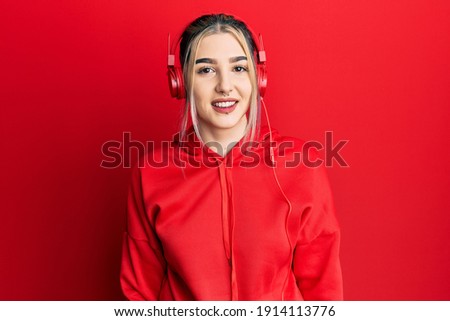 Young modern girl wearing gym clothes and using headphones with a happy and cool smile on face. lucky person. 