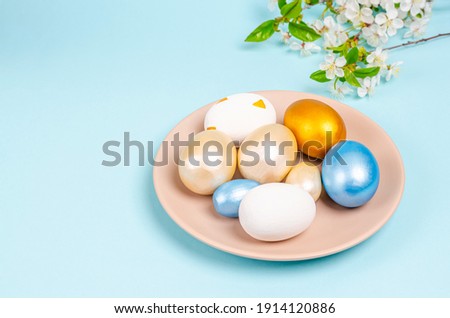 Mother of pearl colored eggs for Easter on a plate on a blue background with copy space. Seasonality concept, spring, postcard, holiday. Flat lay, place for text. Close-up.