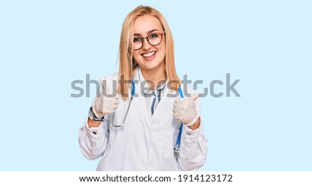 Beautiful caucasian woman wearing doctor uniform and stethoscope success sign doing positive gesture with hand, thumbs up smiling and happy. cheerful expression and winner gesture. 