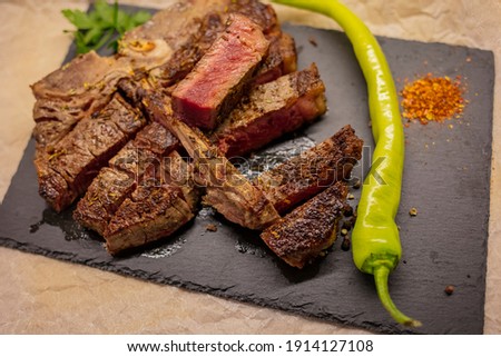 T-bone grilled beef steak with spices and herbs. T-Bone Steak freshly roasted on Barbecue Grill. Delicious T-Bone Steak Medium Roasted with Herbs and Pepper. The steak is on a black plate served 
