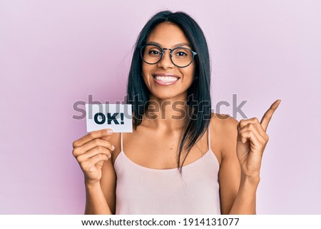 Young african american woman holding ok message paper smiling happy pointing with hand and finger to the side 