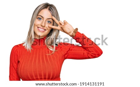 Beautiful blonde woman wearing casual clothes doing peace symbol with fingers over face, smiling cheerful showing victory 