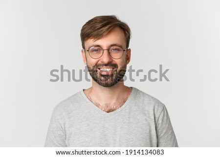 Close-up of handsome modern guy in glasses, smiling and looking at camera, standing over white background