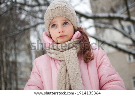 Sad child girl in warm knitted winter clothes spent time outdoors and got frozen.