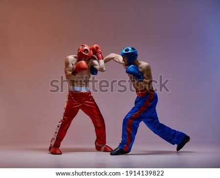 Athletic guys fighting, wearing boxing gloves on red blue studio background with copy space, mixed fight concept