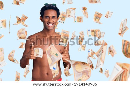 African handsome man wearing swimsuit and sunglasses success sign doing positive gesture with hand, thumbs up smiling and happy. cheerful expression and winner gesture.