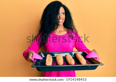 Middle age african american woman holding homemade bread smiling looking to the side and staring away thinking. 