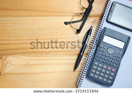 Top view of modern home office workspace, rustic brown desk with mobile phone, calculator, notebook, pen and glasses. Concept of place of study and work, organization and planning.