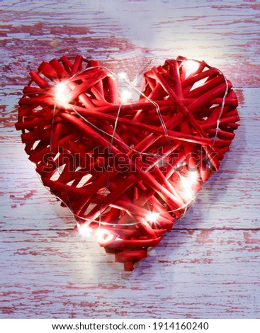 Large red wicker decorative heart close-up on a background of wooden boards. Bright lights shine on it.
