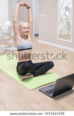 young attractive girl is engaged in fitness at home and looks at the laptop. quarantine fitness concept. high quality