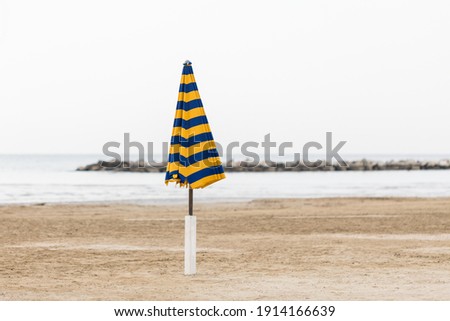 Lonely beach umbrella on empty beach, covered umbrella, beach season is over, summer is over, no sun