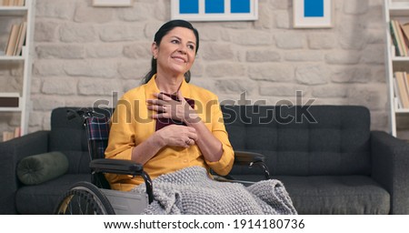 Beautiful old woman in a good mood looking at photos in a wheelchair and smiling. Memories concept.