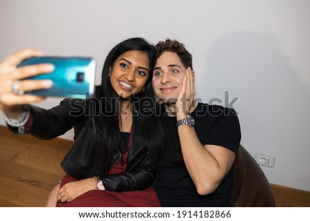 Cheerful young couple take a self portrait with funny face at home sitting on bean bag.