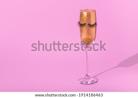 Creative minimal concept with champagne glass of golden glitters and eyelashes on pastel pink background. Abstract celebration and party invitation concept. Copy space