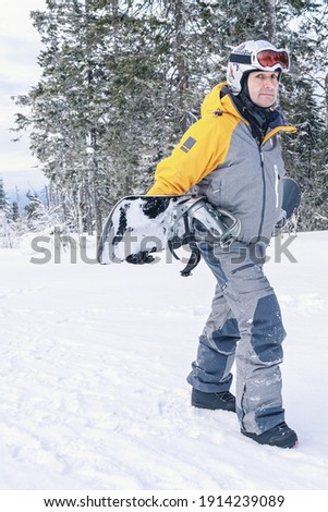 Man with snowboard goes up the mountain on the background of the winter forest. Side view. Vertical shot. Healthy lifestyle. Extreme sports.