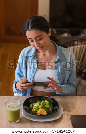 Young brunette woman taking a photo of her salad in her dining room.
