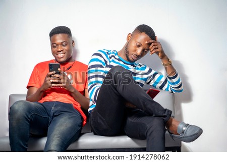 image of african men sitting on a couch, holding smart phone enjoying social media trends-