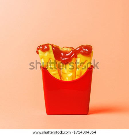Plastic fries drizzled with fresh ketchup on an orange background. 