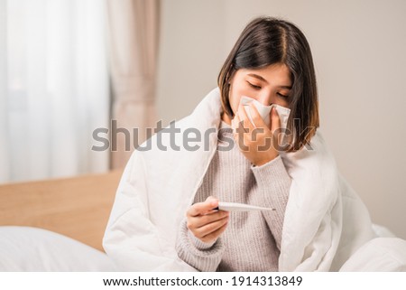 young women have symptom sick and sneezing blowing nose tissue paper with look up to digital thermometer in bedroom  Royalty-Free Stock Photo #1914313849