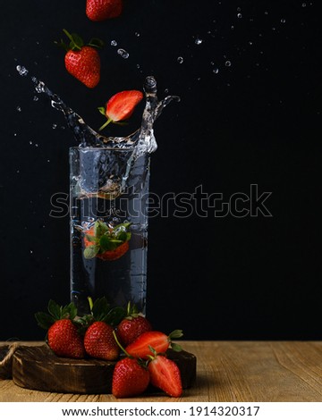 Flying strawberries falls into a glass of water