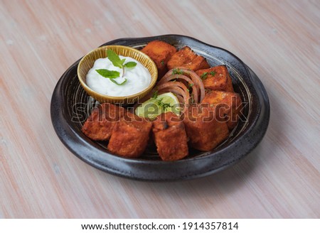 Paneer Ghee Roast Served with Flavored Curd and Mint with Lemon Onion Salad Dressing Side Isometric Close Up View In A Black Bowl