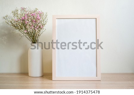 Portrait white picture frame mockup on wooden table. Modern ceramic vase with gypsophila.  White wall background. Scandinavian interior. Vertical. 