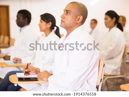 Focused Hispanic man participating in medical congress with colleagues, listening attentively to lecturer