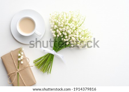 Coffee mug with bouquet of flowers lily of the valley and gift box on white background. Flat lay, top view, copy space.