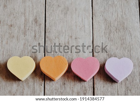 Four heart-shaped sponges are placed on the wooden floor.  There are yellow, orange, pink and purple.  Taken from natural light  There is a blank space for placing text on top of the image.
