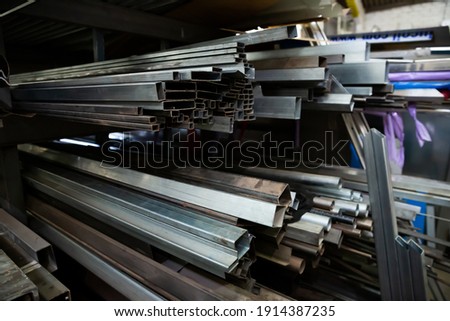 Variety of iron square tubes, round pipes and shaped profiles on rack in metalworking shop.. Royalty-Free Stock Photo #1914387235