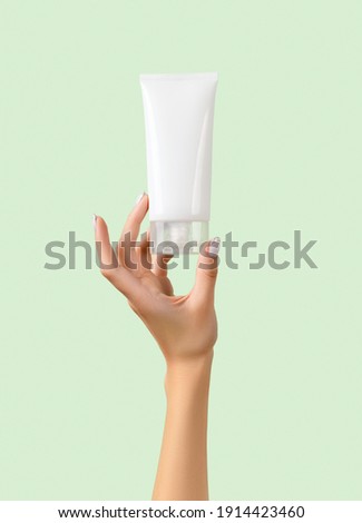 Womans hand holding white tube on pastel green background Royalty-Free Stock Photo #1914423460