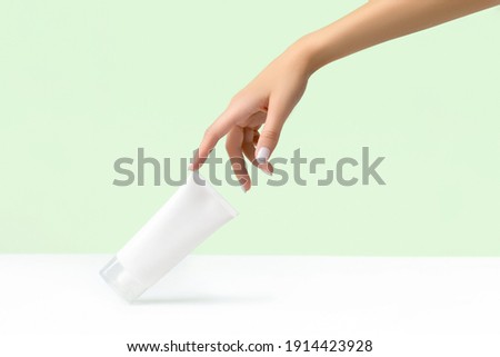Womans hand holding white tube on pastel green background Royalty-Free Stock Photo #1914423928