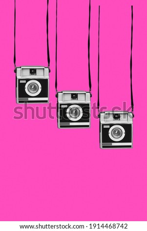 three gray and black retro film cameras, hanging from their strips, on a pink background, with some blank space on the bottom