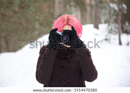Woman with bright pink hair with retro camera in winter forest.